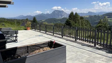 Geräumige Terrasse mit Bergblick, umgeben von einer Holzumzäunung und grüner Landschaft.
