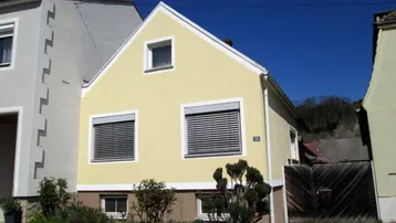 Gelbes Einfamilienhaus mit Satteldach, Rollläden an den Fenstern und kleinem Vorgarten.