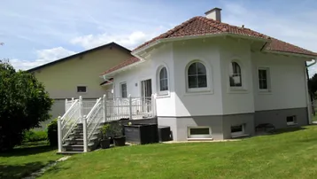 Ansicht des Hauses von der Gartenseite mit Terrasse und gepflegtem Rasen unter blauem Himmel.