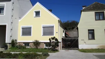Gelbes Einfamilienhaus mit Satteldach und Rollläden an den Fenstern, umgeben von einem kleinen Vorgarten.