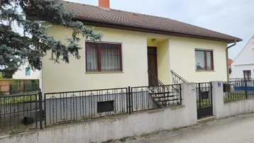 Einfamilienhaus mit gelber Fassade, braunem Dach und Vorgarten an einer ruhigen Straße.