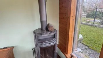 Gemütlicher Wohnbereich mit Kaminofen, Fliesenboden und großem Fenster mit Blick in den Garten.