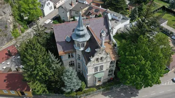 Luftaufnahme einer historischen Villa mit markantem Dach und umliegenden Bäumen in einer Wohngegend.