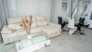 Heller Wohn- und Essbereich mit weißem Sofa, Glastisch und modernen Esszimmerstühlen.