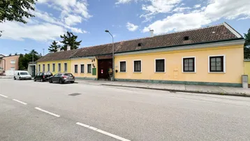 Gelbe Fassade eines traditionellen Gebäudes mit mehreren Fenstern und parkenden Autos davor.