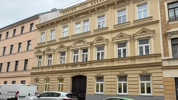 Historisches Gebäude mit klassischer Fassade und verzierten Fenstern an einer Stadtstraße.