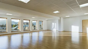 Großer, heller Büroraum mit Holzboden und vielen Fenstern, die viel Tageslicht hereinlassen.
