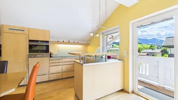 Helle Küche mit Holzelementen, Kochinsel und Zugang zum Balkon mit Bergblick.