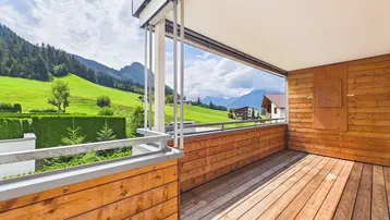 Geräumiger Balkon mit Holzboden und weitem Blick auf die umliegende Berglandschaft und grüne Wiesen.