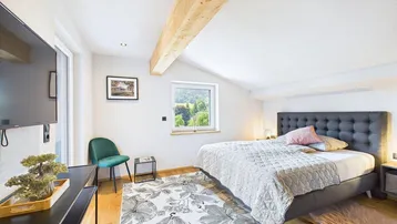 Helles Schlafzimmer mit Holzbalken, gemütlichem Bett und Blick auf die grüne Landschaft.