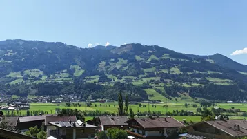 Panoramablick auf das Tal mit grünen Wiesen und majestätischen Bergen im Hintergrund unter blauem Himmel.