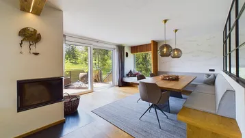 Offener Wohn- und Essbereich mit Kamin, Holzboden und Zugang zu einer sonnigen Terrasse.