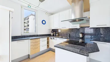 Moderne Küche mit weißen Schränken, dunkler Granitarbeitsplatte und Fensterblick.