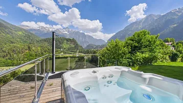 Whirlpool auf einer Holzterrasse mit atemberaubendem Bergblick unter blauem Himmel.