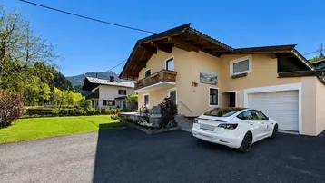 Traditionelles Haus mit Satteldach, Balkon und Garage, umgeben von grüner Landschaft.