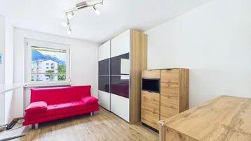Gemütliches Zimmer mit Holzboden, rotem Sofa und Bergblick aus dem Fenster.