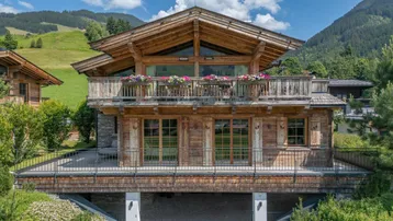 Traditionelles Holzchalet mit Balkonen und Bergblick, eingebettet in eine grüne Landschaft.