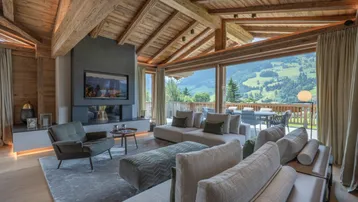 Großzügiges Wohnzimmer mit Holzbalkendecke, Kamin und bodentiefen Fenstern mit Bergblick.