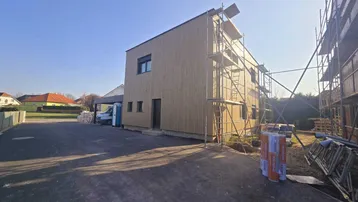 Neubau mit Holzfassade und Gerüst, noch im Bau befindlich an einem sonnigen Tag.