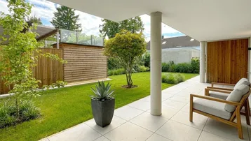 Moderne Terrasse mit Sitzgelegenheiten, angrenzendem Rasen und gepflegtem Gartenbereich.