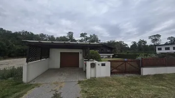 Einfahrt zum Haus mit Carport und Garage, umgeben von Grünflächen und einem Holzzaun.