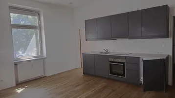 Moderne Einbauküche in Dunkelgrau mit Holzboden und Fenster, bereit zur Nutzung.