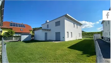 Modernes weißes Einfamilienhaus mit gepflegtem Rasen und klarem blauen Himmel.