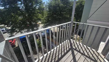 Balkon mit Holzfußboden und Metallgeländer, bietet einen Blick auf Bäume und parkende Autos.