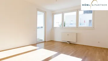 Helles Zimmer mit Holzboden, großen Fenstern und Zugang zu einem Außenbereich, durchflutet von Sonnenlicht.