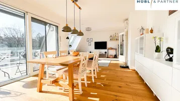 Heller Wohn- und Essbereich mit Holzboden, großem Esstisch und Zugang zu einem sonnigen Balkon.