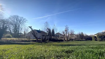 Weitläufige Grünfläche mit frischem Gras und Häusern im Hintergrund unter strahlend blauem Himmel.