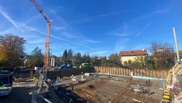 Baustelle mit Fundamentarbeiten, Bewehrung und Kran unter blauem Himmel.