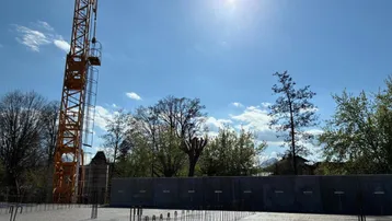Baustelle bei sonnigem Wetter mit Kran und vorbereitetem Fundament für ein neues Gebäude.