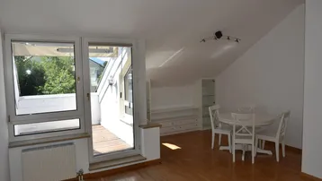 Helles Wohn- und Esszimmer mit Holzboden, Dachschrägen und Zugang zu einem Außenbereich.