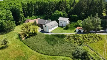 Luftaufnahme des Anwesens mit mehreren Gebäuden, umgeben von grünen Wiesen und dichtem Wald.