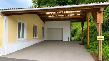Gelbes Haus mit überdachtem Carport und Garagentor, umgeben von viel Grün.