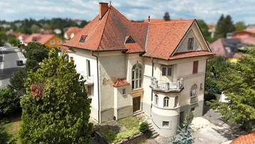 Historische Villa mit markantem Ziegeldach und umliegender Grünfläche in einer Wohngegend.