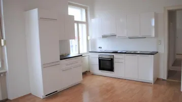 Helle Küche mit weißen Schränken, dunkler Arbeitsplatte, integriertem Backofen und Laminatboden.