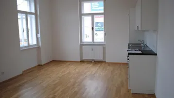 Heller Wohnbereich mit Parkettboden und integrierter Küchenzeile, ideal für offenes Wohnen.