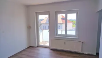 Helles Zimmer mit Laminatboden, weiß gestrichenen Wänden und Zugang zu einem kleinen Balkon.