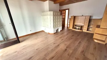 Gemütliches Wohnzimmer mit traditionellem Kachelofen, Holzbalkendecke und Laminatboden.