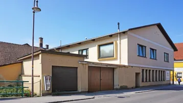 Ansicht des Gebäudes von der Straße mit Garagentoren und Fenstern unter blauem Himmel.