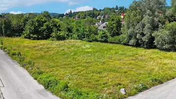 Großes, unbebautes Grundstück an einer Straßenecke mit viel Grün und Häusern im Hintergrund.