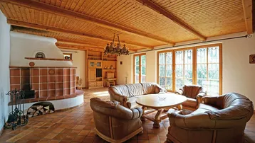 Gemütliches Wohnzimmer mit traditionellem Kachelofen, Holzbalkendecke und Terrakotta-Fliesenboden.