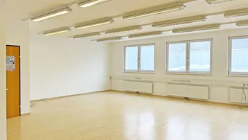 Leerer, heller Raum mit vielen Fenstern, Holzfußboden und Deckenleuchten, ideal für Büro oder Gewerbe.