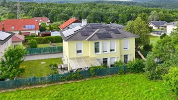 Gelbes Einfamilienhaus mit Solaranlage auf dem Dach und großem Garten in ländlicher Umgebung.