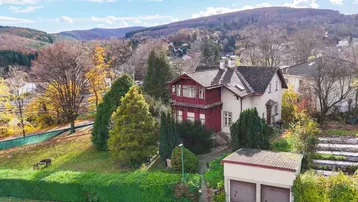 Charmantes Altbauhaus mit roter Fassade, umgeben von einem gepflegten Garten und herbstlicher Berglandschaft.