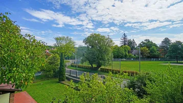 Weitläufiger Blick über grüne Felder und Bäume unter einem blauen Himmel.
