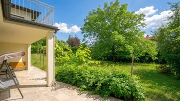 Gedeckte Terrasse mit Fliesenboden und Schaukelbank, umgeben von viel Grün.