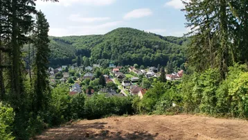 Panoramablick über eine bewaldete Hügellandschaft mit einem Dorf im Tal unter blauem Himmel.